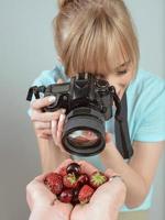 joven fotógrafa disparando con cámara digital fresas y cerezas en las manos. primer plano, tiro, hobby, comida, concepto de profesión