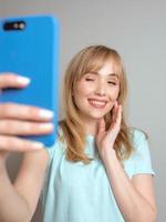 stylish beautiful blonde woman blogger making selfie with her smartphone by the window. Trend, technology, beauty, fashion concept photo