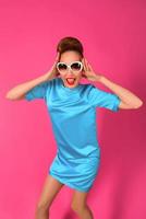 portrait of young beautiful woman in blue silk dress and white sunglasses ot the pink background photo