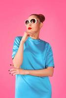 portrait of young beautiful woman in blue silk dress and white sunglasses ot the pink background photo