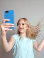 elegante hermosa mujer rubia blogger haciendo selfie con su teléfono inteligente junto a la ventana. tendencia, tecnología, belleza, concepto de moda. foto