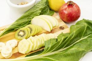 A kitchen cutting board with kiwifruit apples and cucumbers on top photo