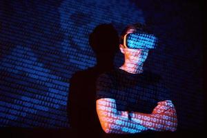 Double exposure of a caucasian man and Virtual reality headset is presumably a gamer or a hacker cracking the code into a secure network or server, with lines of code photo