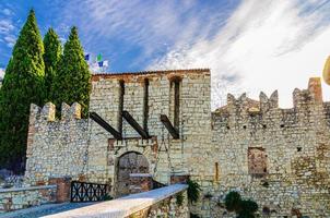 Brescia, Italy, September 11, 2019 Stone wall with merlons and drawbridge Gate of medieval Castle Brescia photo