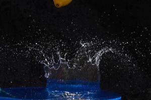 limón amarillo cayendo en el agua azul sobre un fondo negro foto