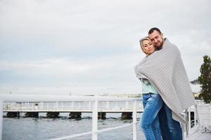 Happy young couple in a blanket, standing on the pier in the water. photo