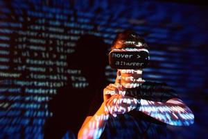 Double exposure of a caucasian man and Virtual reality headset is presumably a gamer or a hacker cracking the code into a secure network or server, with lines of code photo