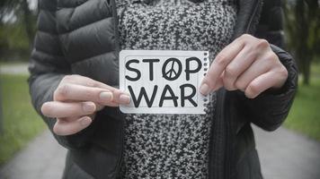 Approach to the hands of a Hispanic woman in the middle of a park holding in her hands a paper with the message STOP WAR photo