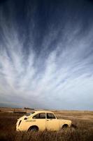 Wispy clouds over abandoned foreign made car