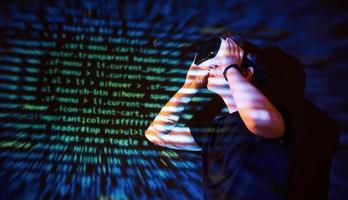 Double exposure of a caucasian man and Virtual reality headset is presumably a gamer or a hacker cracking the code into a secure network or server, with lines of code photo