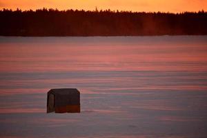 Icefishing shack on frozen lake at sunset photo