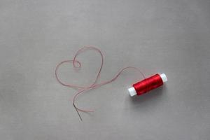 Red thread from the spool, laid out in the shape of a heart, with a needle at the end. photo