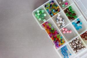 Multi-colored beads in the organizer slots, prepared for jewelry and decor, on gray background. Top view. With copy space