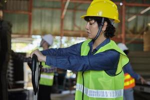 Female warehouse worker in safety uniform and hard hat works by hydraulic jack lift piles of cardboard for shipping and logistic transport at manufacture factory, supply packaging stocks industrial. photo