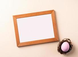 Wooden frame with colored easter egg flat lay on beige background photo