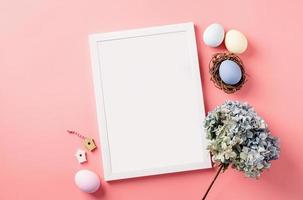 White photo frame with easter decorations flat lay on pink background