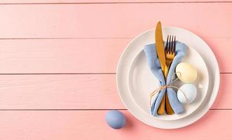 Table setting for Easter feast. Easter eggs, tulips and cutlery top view flat lay on pink rustic background photo