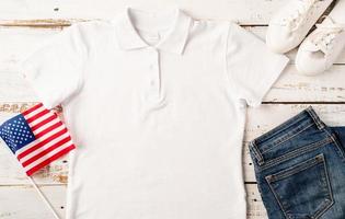 Mockup design white polo t shirt for logo, top view on white wooden background with US flag, shoes and jeans photo