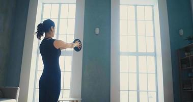 brünette frau im trainingsanzug macht sportübungen mit gewichtsplatte in der nähe des sofas im wohnzimmer zu hause zeitlupe video