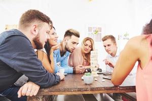 Group of creative friends sitting at wooden table. People having fun while playing board game photo