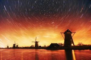 Colorful spring night with traditional Dutch windmills canal in Rotterdam. Wooden pier near the lake shore. Holland. Netherlands. Fantastic starry sky and the milky way photo