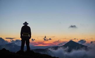 hombre parado en una cornisa de una montaña, disfrutando de la hermosa puesta de sol foto