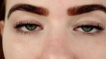 jonge vrouw ogen van grijze kleur met professionele make-up op wenkbrauwen onder helder elektrisch licht slow motion macro video