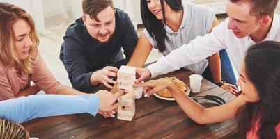 Group of creative friends sitting at wooden table. People having fun while playing board game photo