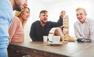 Group of creative friends sitting at wooden table. People having fun while playing board game photo