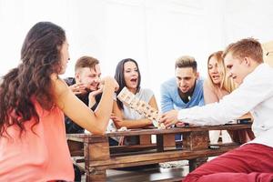 Group of creative friends sitting at wooden table. People having fun while playing board game photo