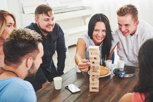 Group of creative friends sitting at wooden table. People having fun while playing board game photo