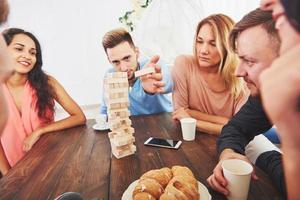 Group of creative friends sitting at wooden table. People having fun while playing board game photo