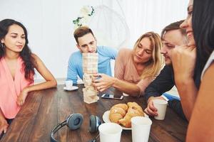 Group of creative friends sitting at wooden table. People having fun while playing board game photo