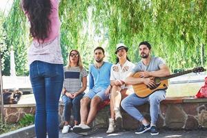 grupo de amigos felices con guitarra. mientras uno de ellos toca la guitarra y otros le dan un aplauso foto