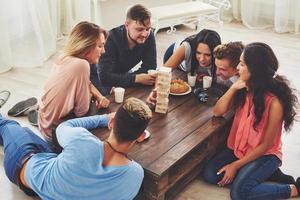 Group of creative friends sitting at wooden table. People having fun while playing board game photo