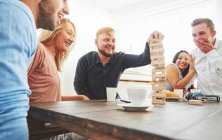 Group of creative friends sitting at wooden table. People having fun while playing board game photo