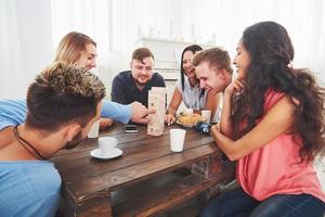 Group of creative friends sitting at wooden table. People having fun while playing board game photo