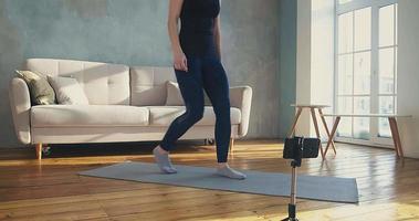 Pretty woman model adjusts mobile phone and shows plank pose shooting video in living room at home during quarantine slow motion