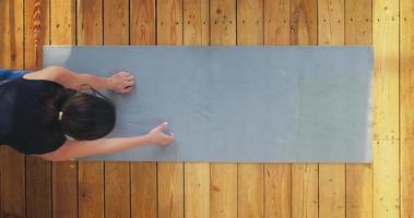 Graceful young woman in comfortable tracksuit stands in plank pose on wooden floor in light room view from above slow motion video