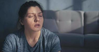 Tired young woman in grey t-shirt lit by sunlight rests breathing heavily after intensive training in room closeup slow motion video