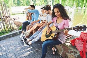 Group of happy friends with guitar. While one of them is playing guitar and others are giving him a round of applause photo