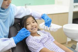 una niña linda con los dientes examinados por un dentista musulmán en la clínica dental, revisión de dientes y concepto de dientes sanos