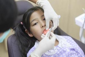 una niña linda con los dientes examinados por un dentista en una clínica dental, un chequeo dental y un concepto de dientes sanos foto