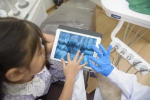 mujer dentista explicando la radiografía de los dientes a una niña en la clínica dental, chequeo dental y concepto de dientes sanos foto