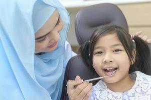 una niña linda con los dientes examinados por un dentista musulmán en la clínica dental, revisión de dientes y concepto de dientes sanos foto