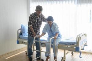 Senior man helping cancer patient woman wearing head scarf with walker at hospital, health care and medical concept photo