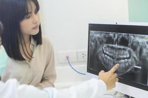 un dentista explicando la radiografía de los dientes a una mujer en la clínica dental, el chequeo dental y el concepto de dientes sanos foto