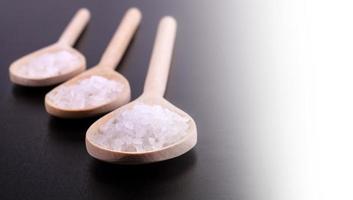 Bath salt in three wooden spoons on a dark polished desk in backlight