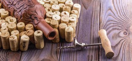 Clay bottle, metal corkscrew and cork on a wooden table. photo