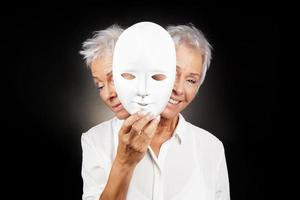 mujer mayor escondiendo la cara feliz y triste detrás de la máscara
